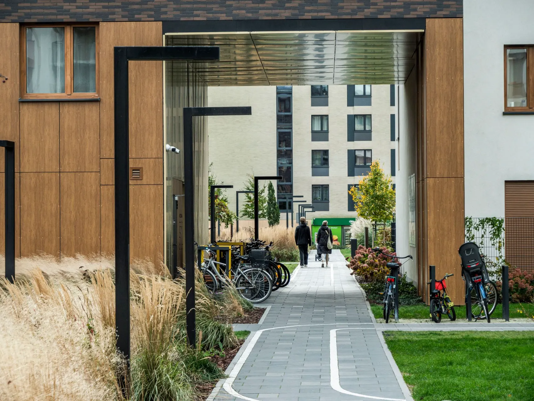 A landscaped walkway running between two contemporary apartment buildings, with planted beds and bicycle parking