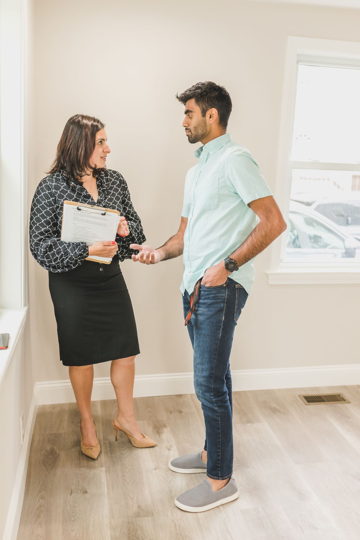 A leasing agent holding a clipboard, talking with a prospective renter in an empty apartment