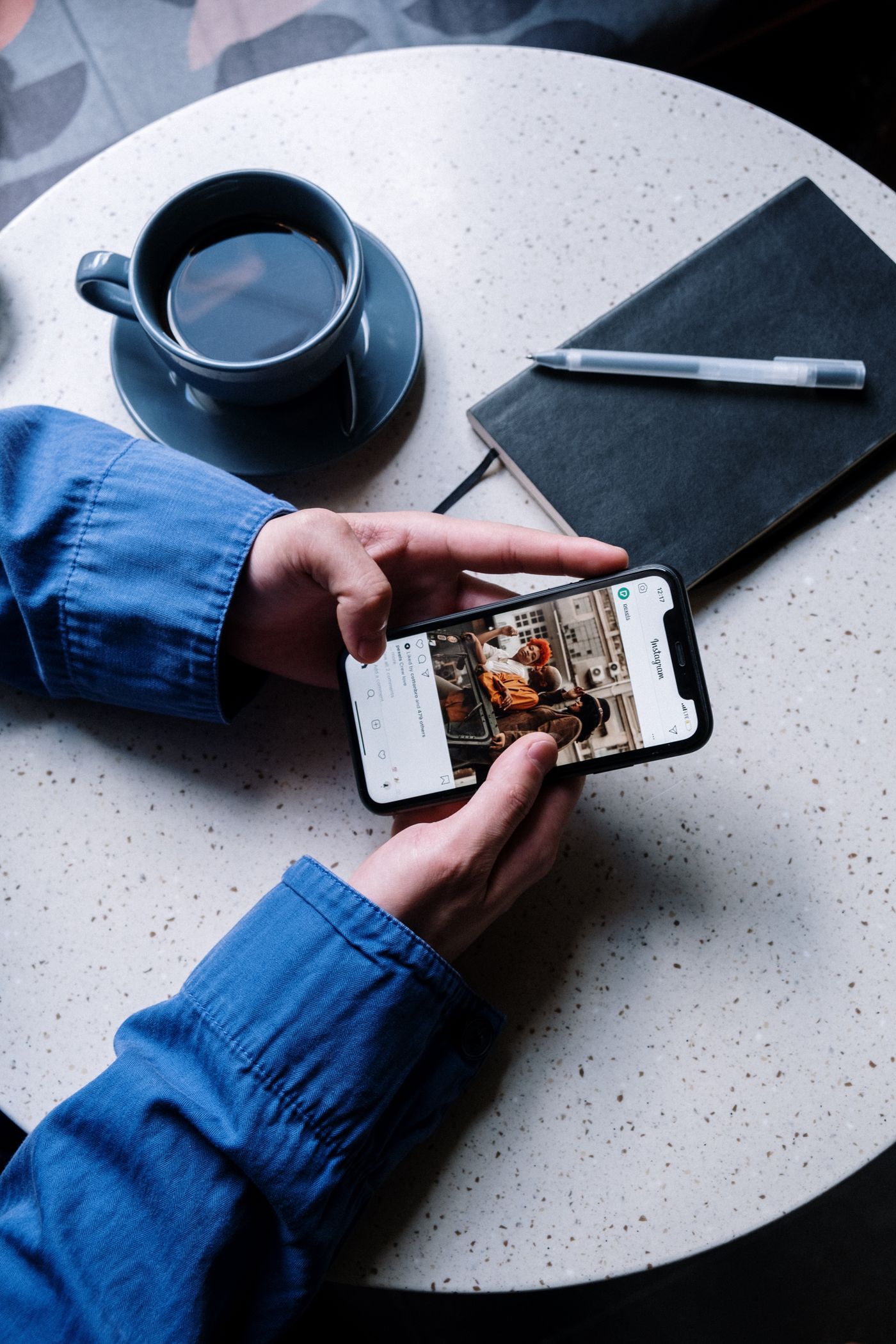 Hands scrolling an Instagram feed on a phone at a café table, next to a cup of coffee